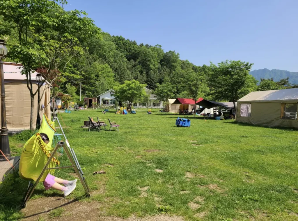 잔디광장 옆으로 텐트와 타프가 설치되어있고, 아이는 해먹그네에 앉아 쉬고있음.